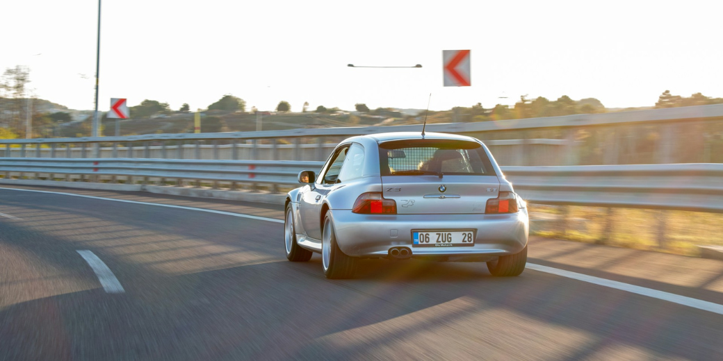 Silver hatchback car driving on highway at sunset, showcasing the need for jump boxes as a safety net for motorists on the go.