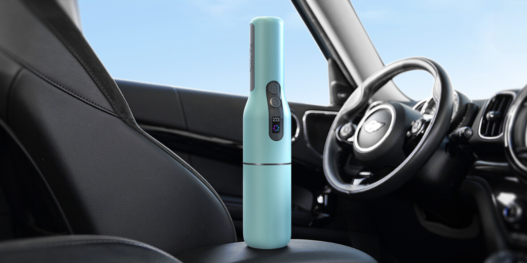 A compact, pastel green handheld vacuum cleaner standing upright on the passenger seat inside a car.
