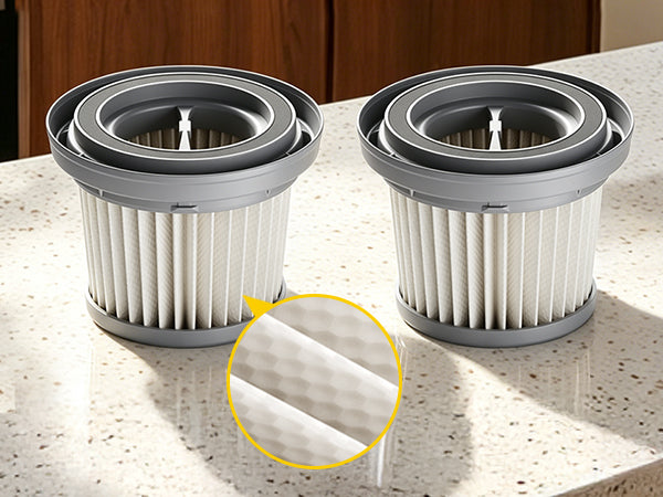 Two pleated white and gray vacuum filter cartridges displayed on a speckled countertop, with a yellow circular inset highlighting the filter material texture.