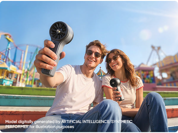 Two people holding GoFlow 11 Apex Handheld Fan in front of an amusement park.