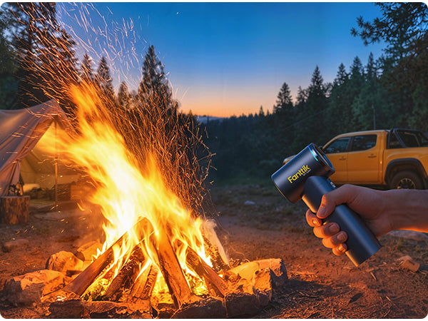 Person holding a Fanttik electric air duster near a campfire with a tent and vehicle in the background.