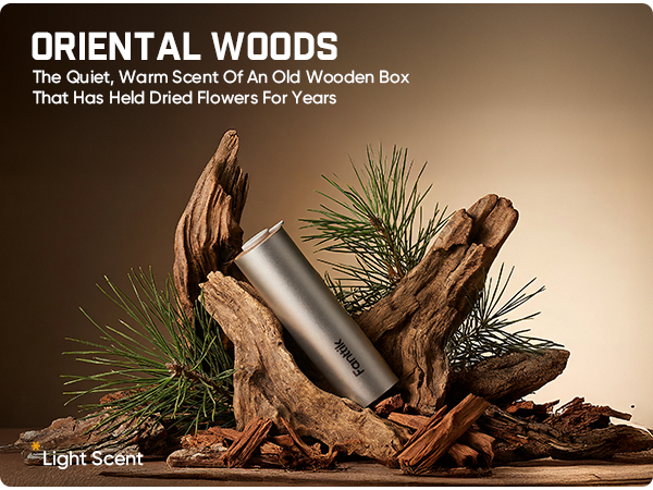 A silver cylindrical bottle labeled 'torric' displayed among driftwood, pine needles, and wood chips on a wooden surface, with the text 'ORIENTAL WOODS' and 'The Quiet, Warm Scent Of An Old Wooden Box That Has Held Dried Flowers For Years' on a warm brown gradient background.