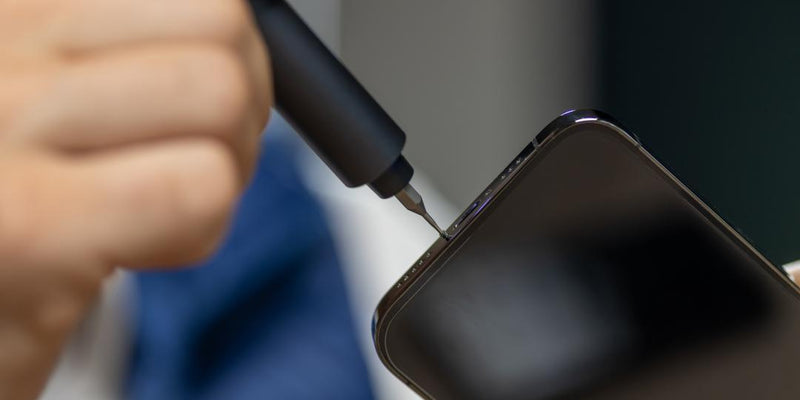 Hand using a compact electric screwdriver (precision screwdriver) to remove a smartphone screw — portable cordless electric screwdriver for DIY electronics repair.