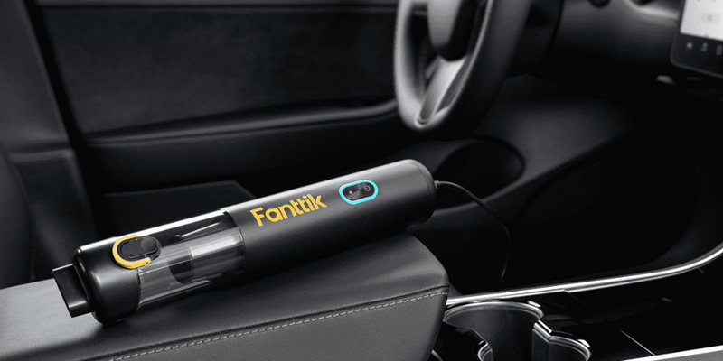 Compact Fanttik cordless car vacuum resting on a black leather center console, illustrating the environmental heat stress tools face in vehicle interiors.
