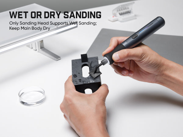 A person's hands are shown using a dark gray rotary sanding tool on a black sanding block on a white workbench. The image includes text overlays explaining the wet or dry sanding feature and shows the sanding head detached in the background.