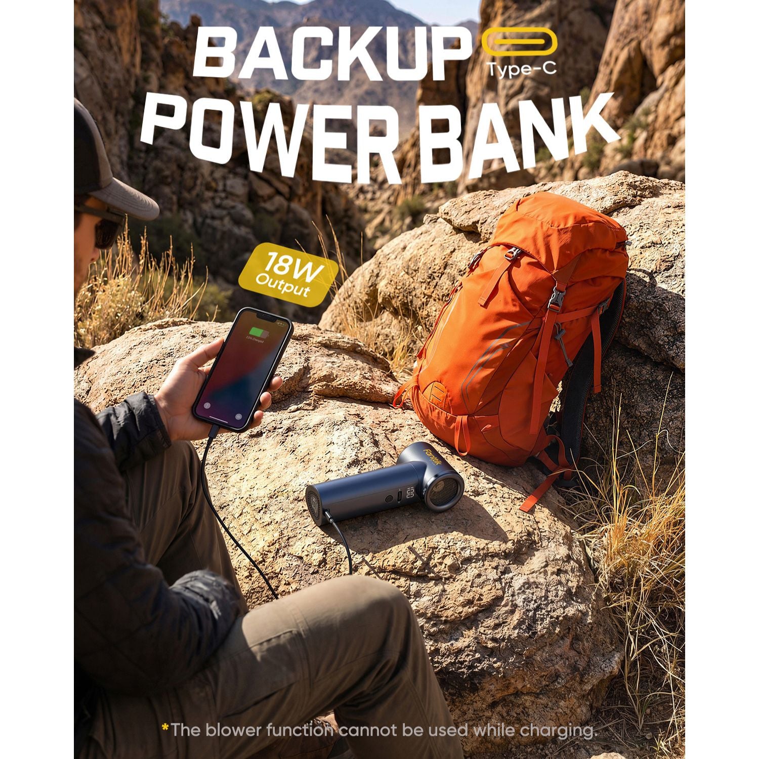 Person using a power bank in a desert setting with an orange backpack and a blower on a rock.