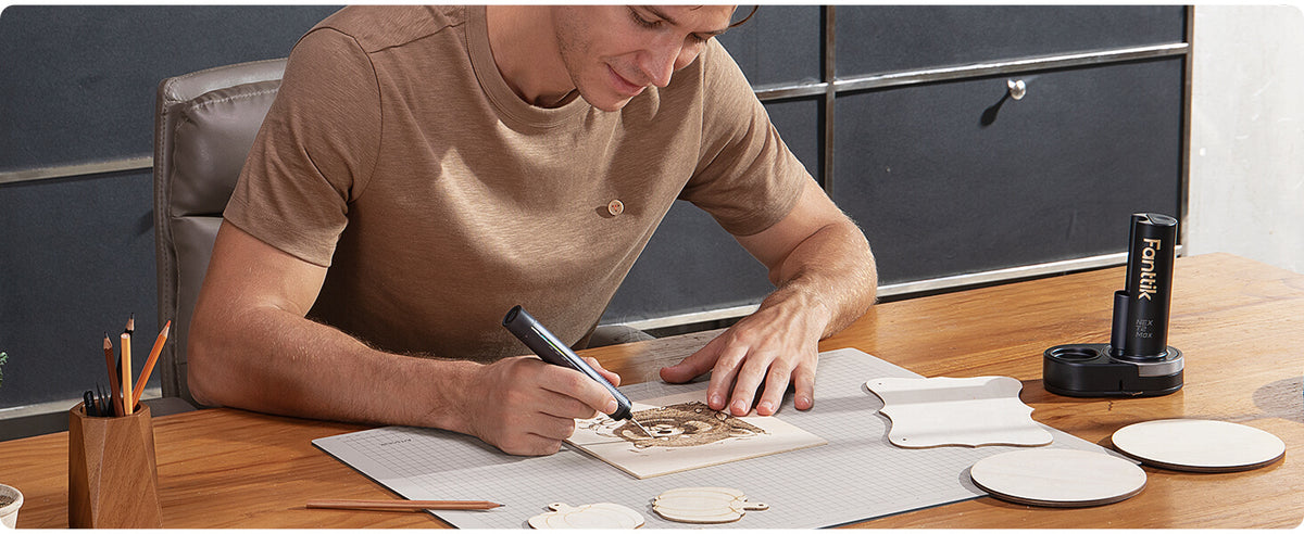 A man in a brown t-shirt sits at a wooden desk, using a black Soldering Iron on a square piece of plank. 