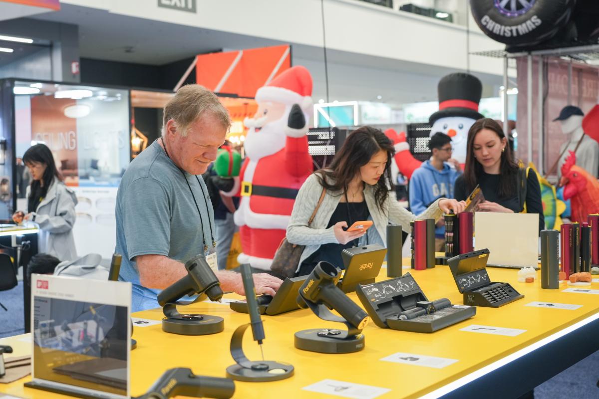 People interacting with display models of calculators and electronic devices at a trade show.