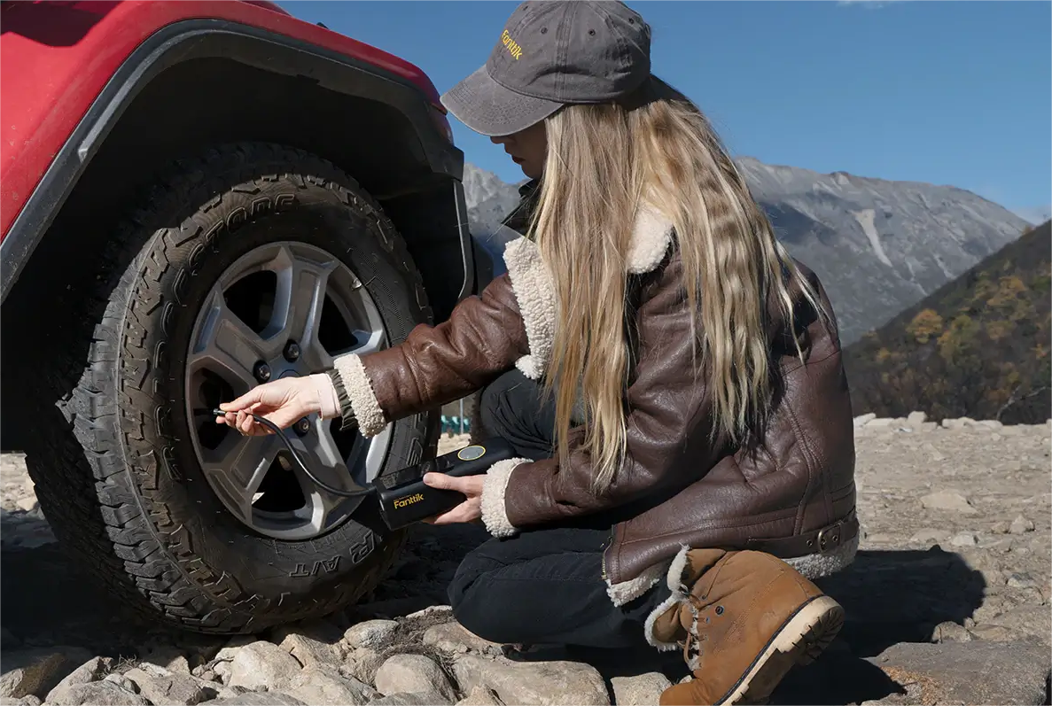 A person crouching down to inflate a Jeep Wrangler's tire using a Fanttik portable tire gauge with pumping function