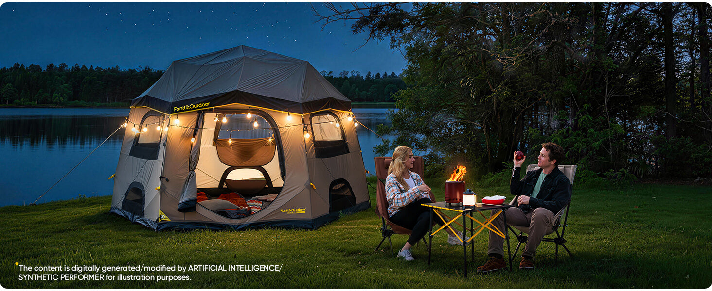A large pop-up camping tent with warm interior lights is pitched on a grassy lakeside at dusk, with two people sitting nearby by a small table and fire. Trees and water are visible in the background.